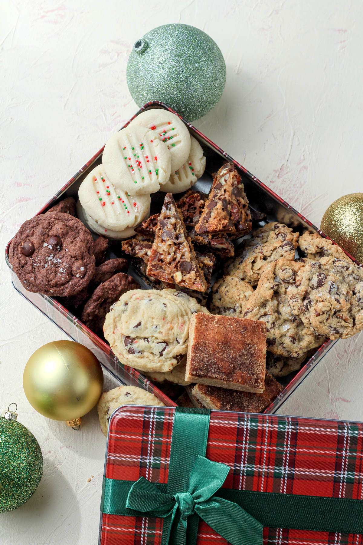 A top down photo of a red and green cookie tin filled with Christmas cookies.