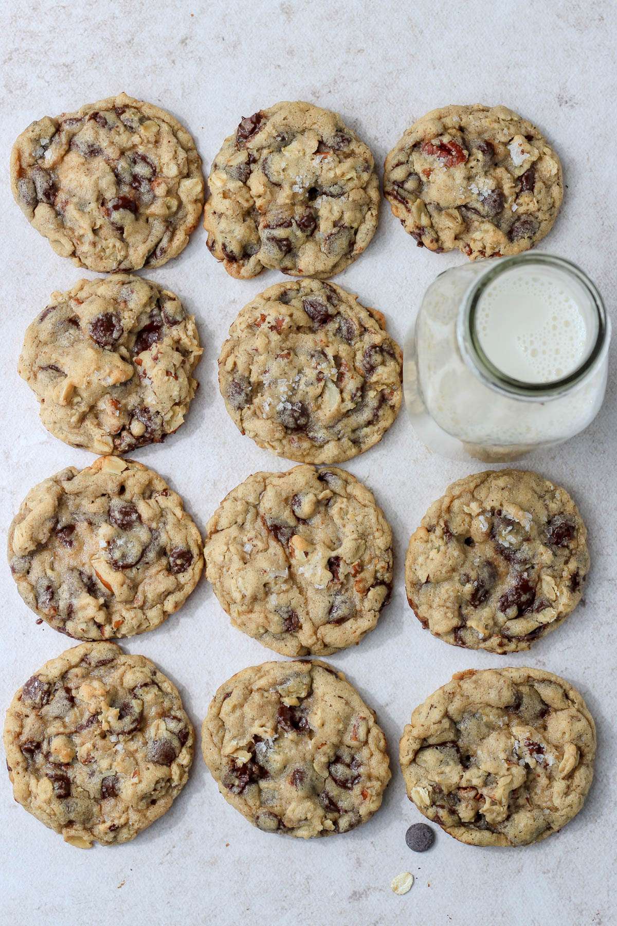 A 3 by 4 grid of eleven cowboy cookies with a glass jug of milk replacing a cookies spot on the second row far right side.