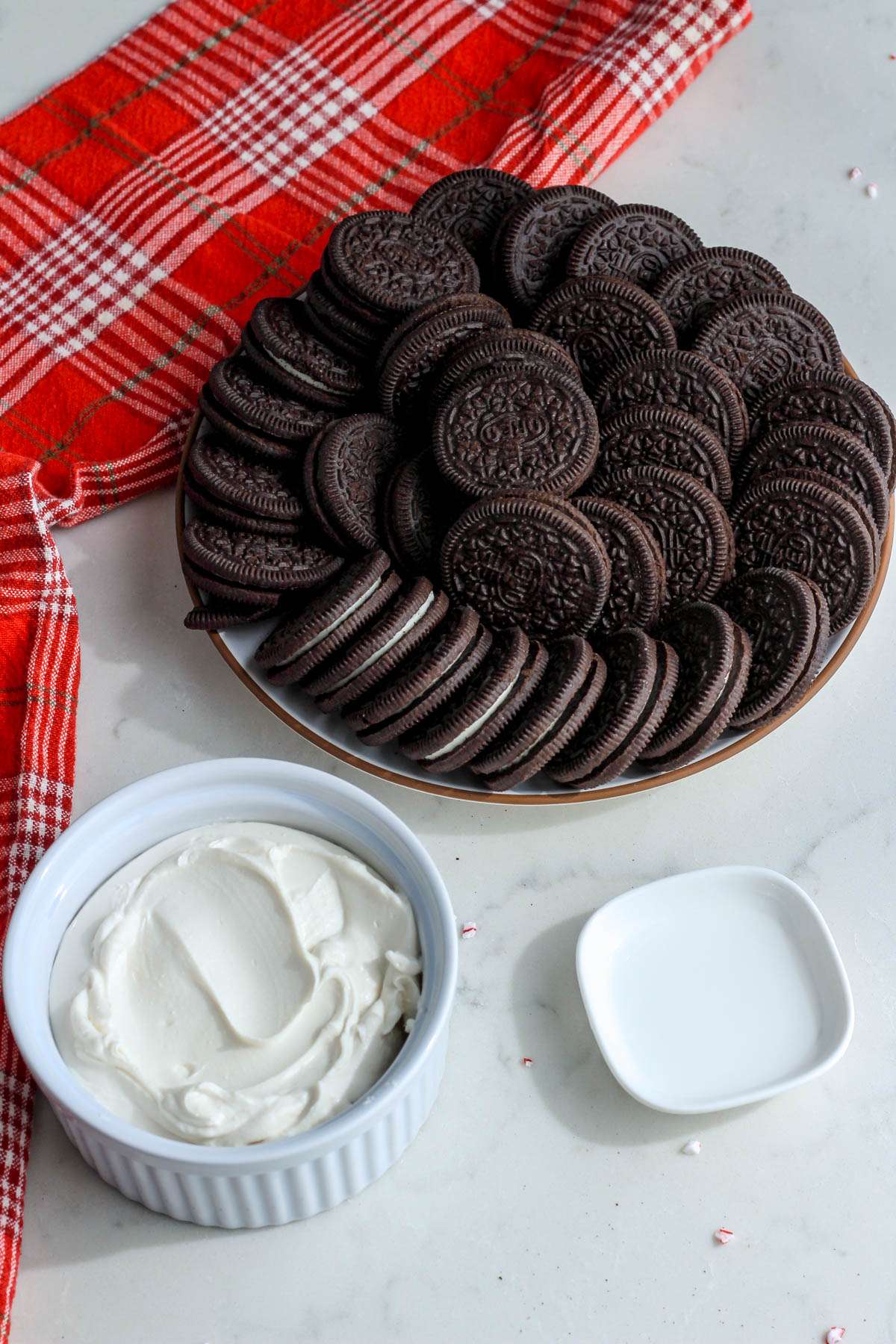 Ingredients for peppermint Oreo truffles on a white counter with a red dish towel.