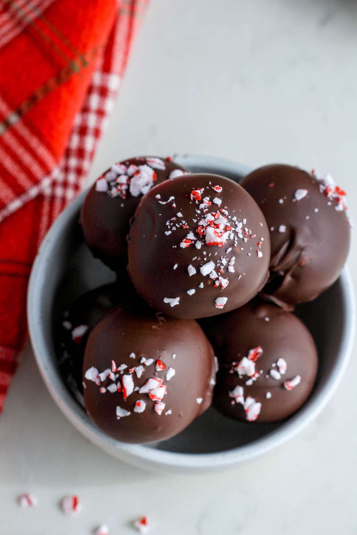 A top down picture of a small white bowl filled with peppermint oreo truffles on a white counter.