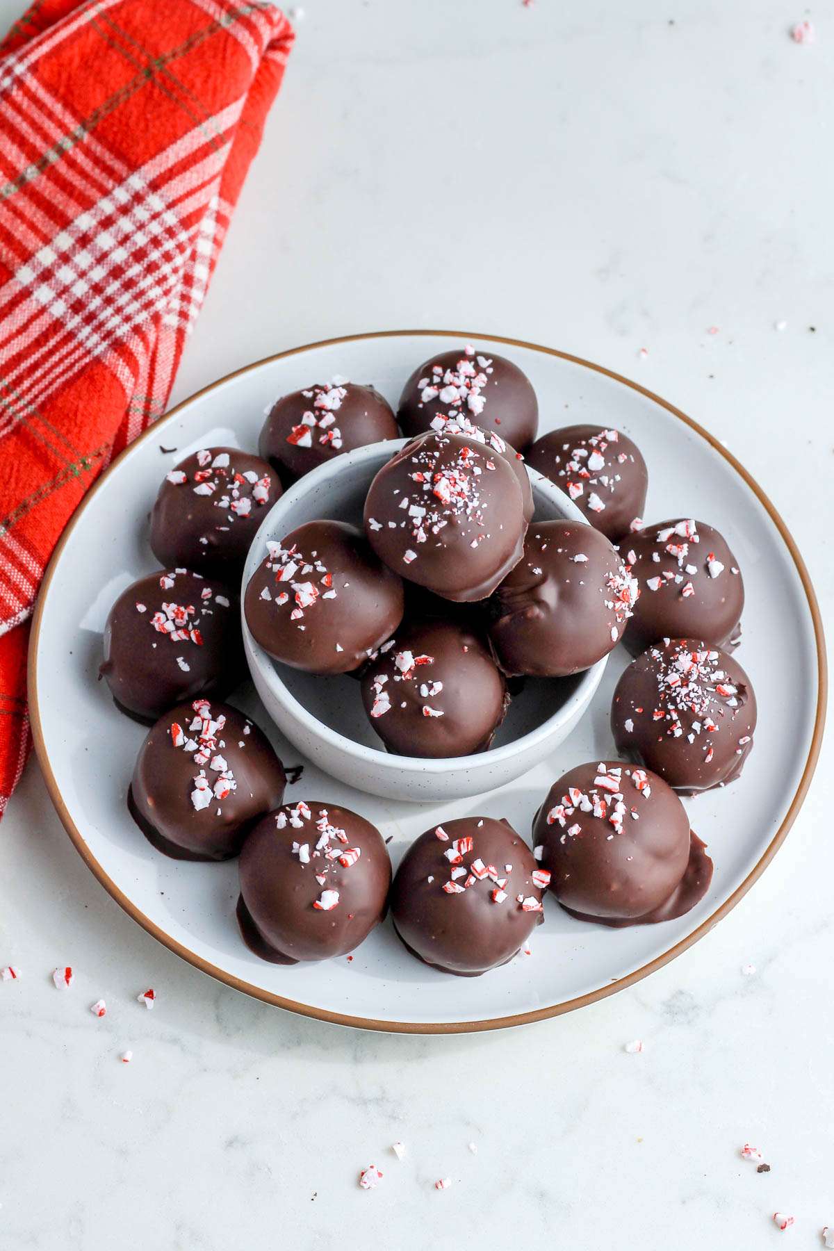 A white plate with a small white bowl in the middle topped with peppermint oreo truffles.