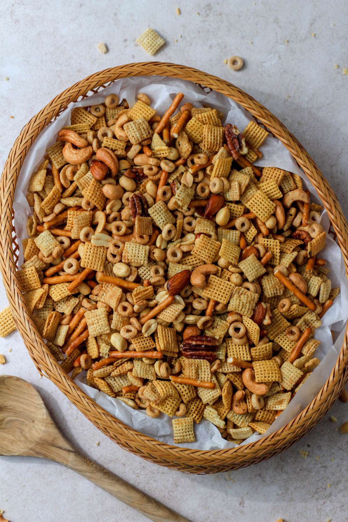 A large whicker basket filled with a parchment paper piece and dairy-free Chex party mix next to a wooden spoon.
