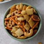 A close up of a small green bowl filled with dairy-free Chex party mix on a cream counter.