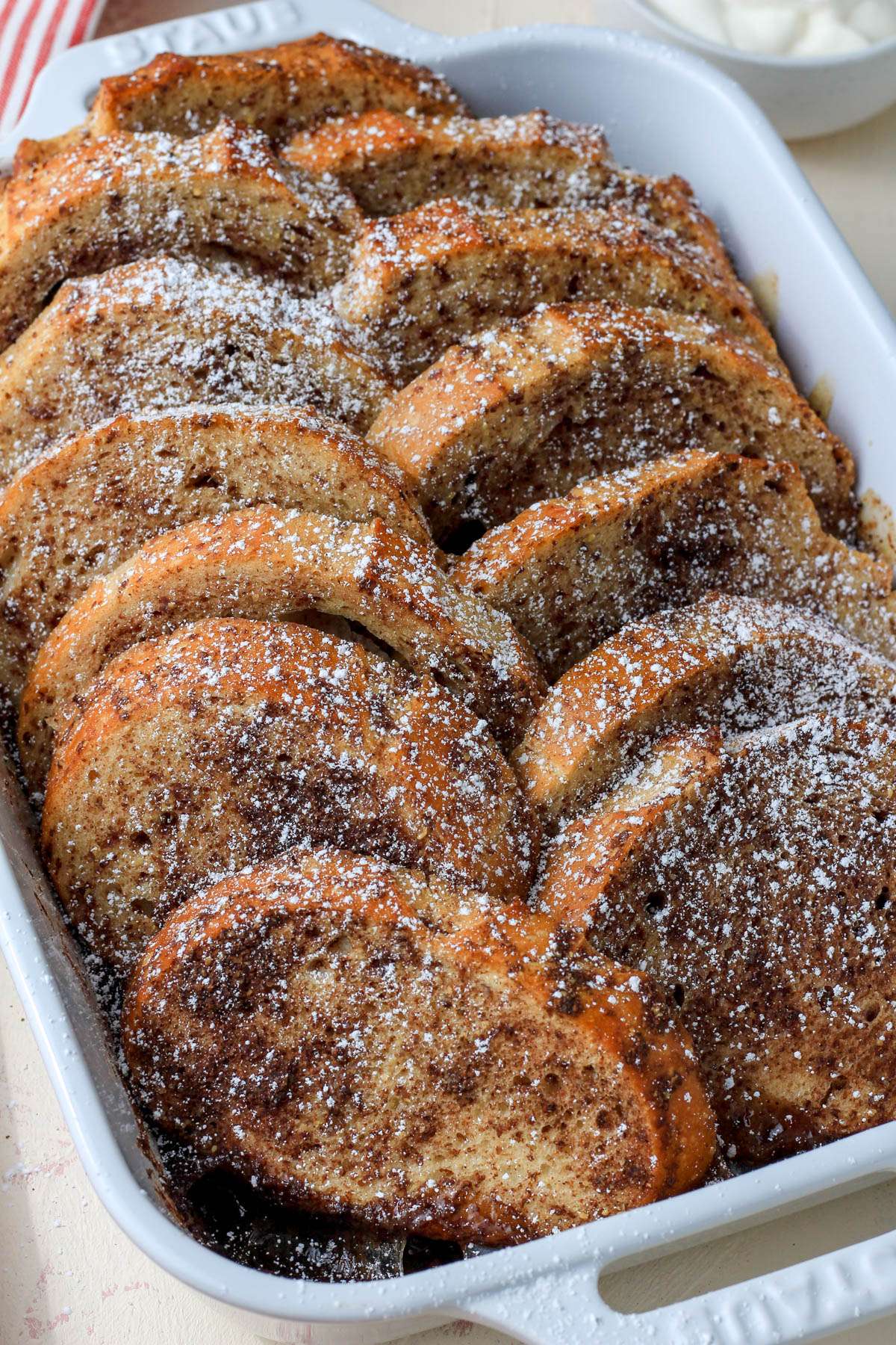 A white baking pan with vegan overnight french toast casserole dusted with powdered sugar.