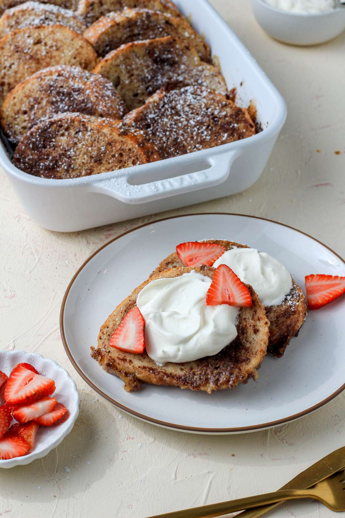 A white and brown plate topped with two slices of vegan french toast topped with vegan whipped cream and strawberries.