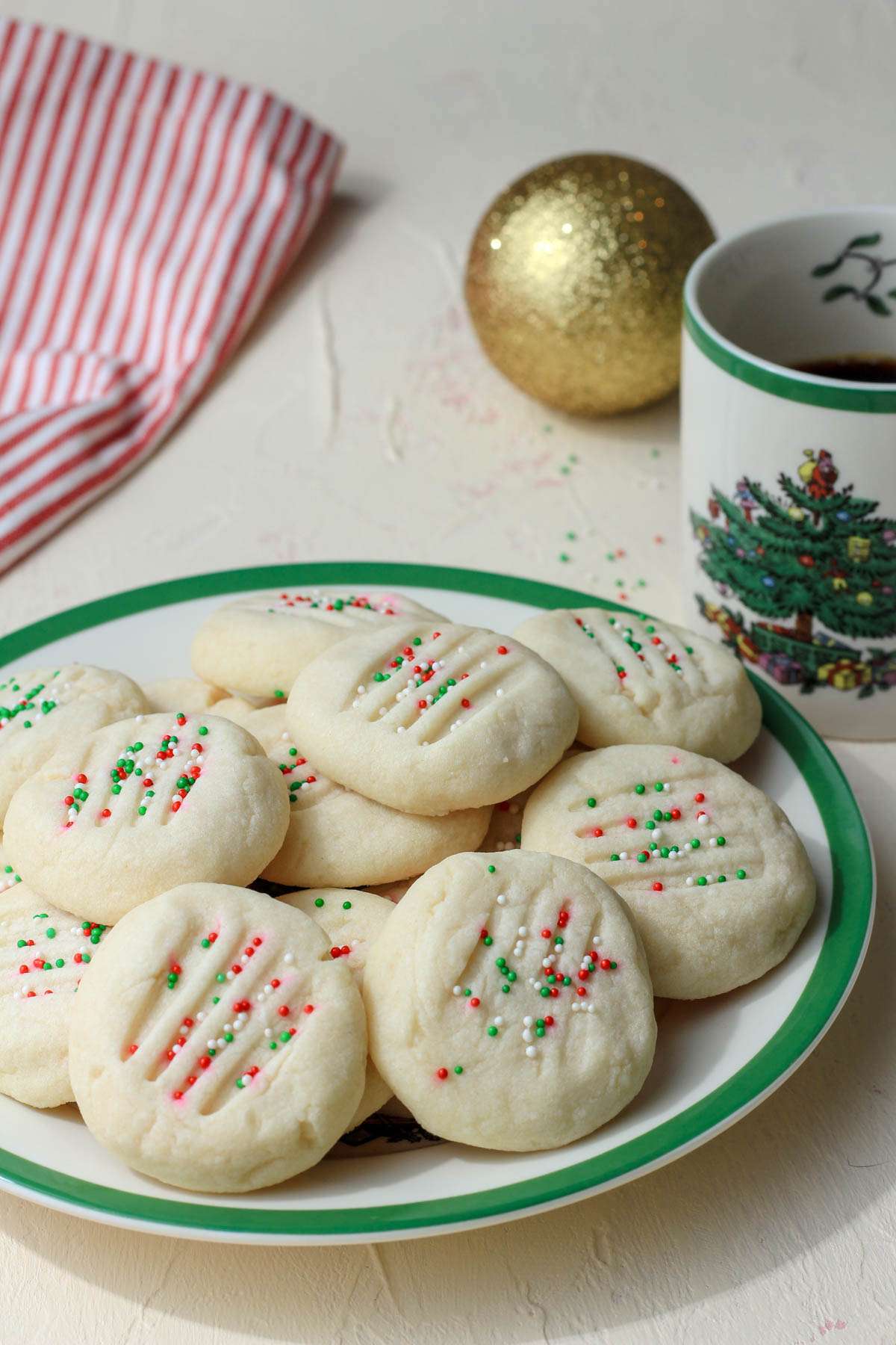 A white and green Christmas plate topped with easy whipped shortbread cookies and a christmas tree cup of coffee.