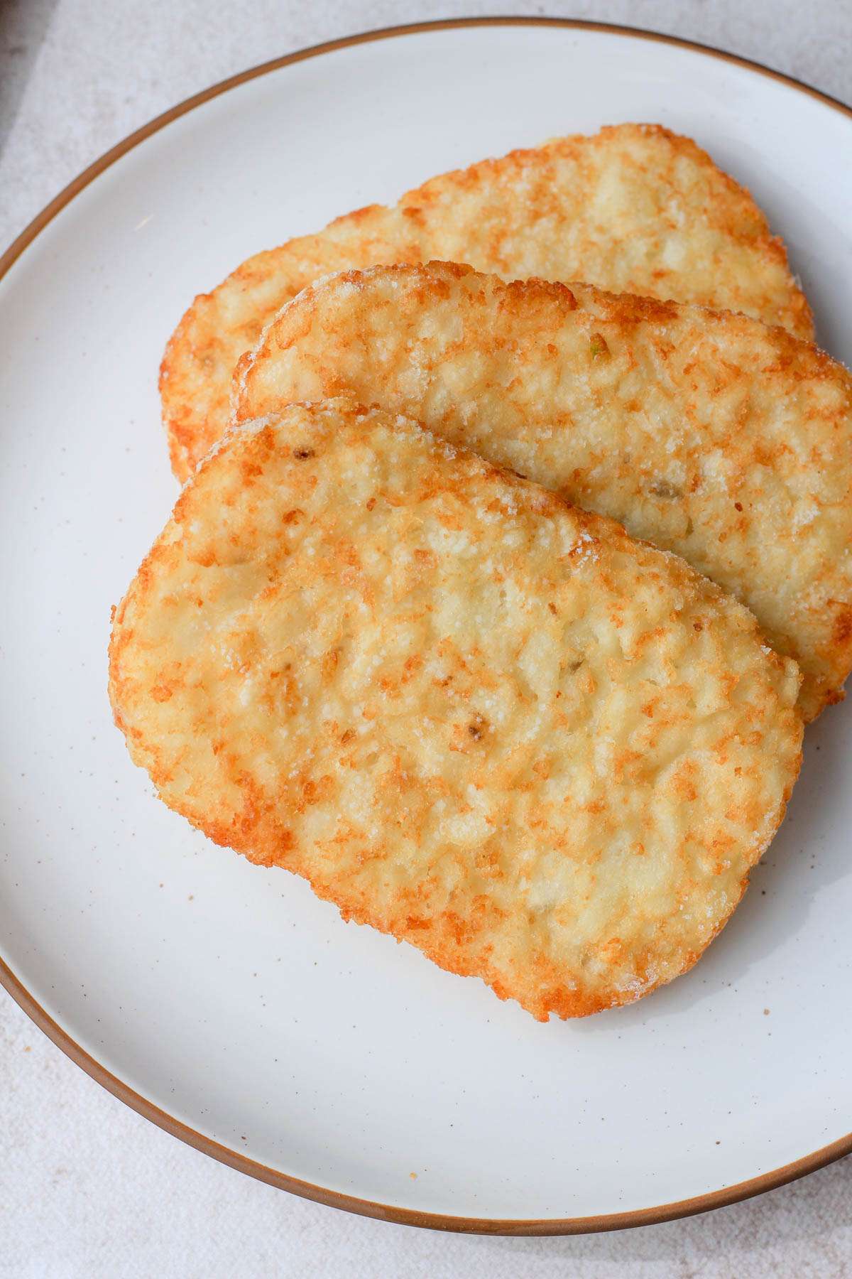 A white plate with a brown rim and three frozen hash browns.