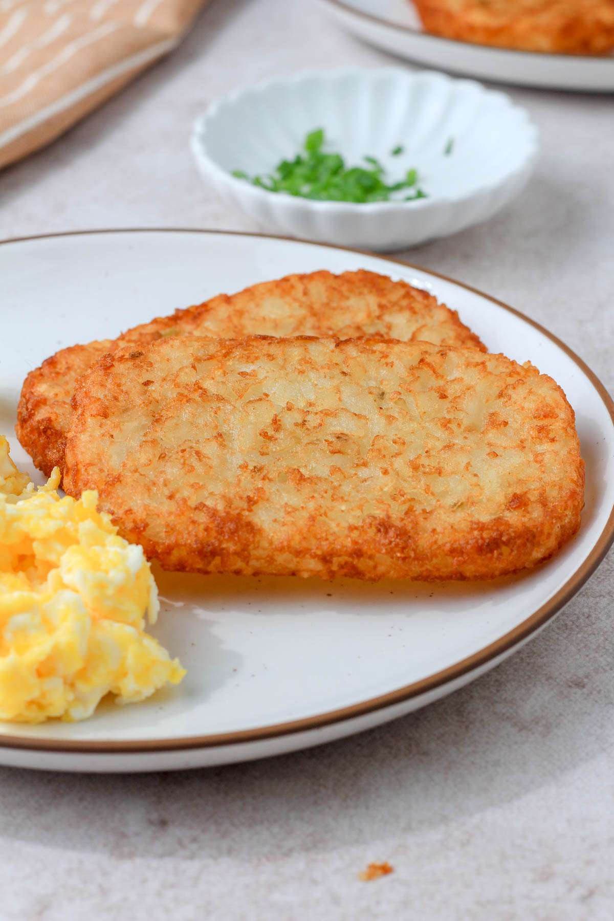 A white plate with a brown rim with two golden hash browns next to a small pile of scrambled eggs.