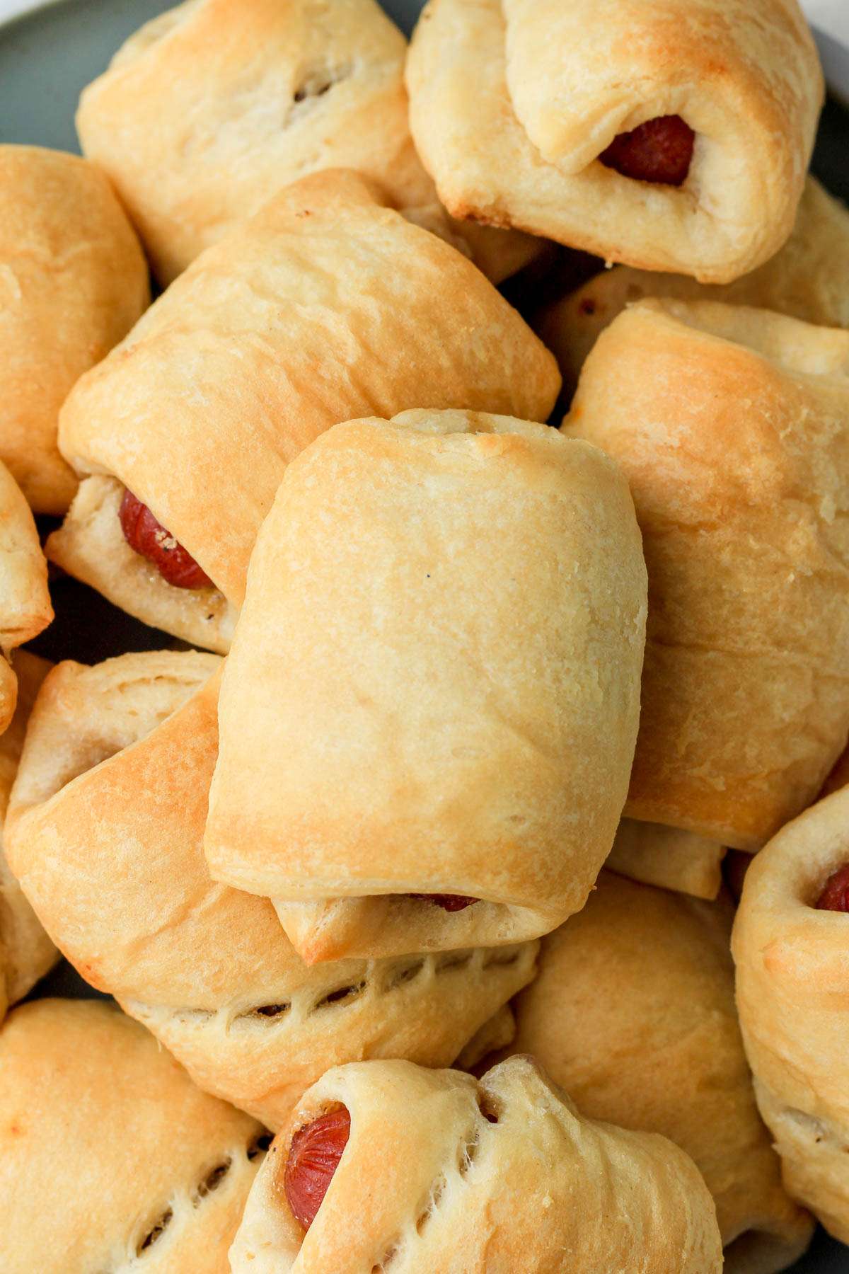 A top down image of a pile of bacon wrapped pigs in a blanket on a plate.