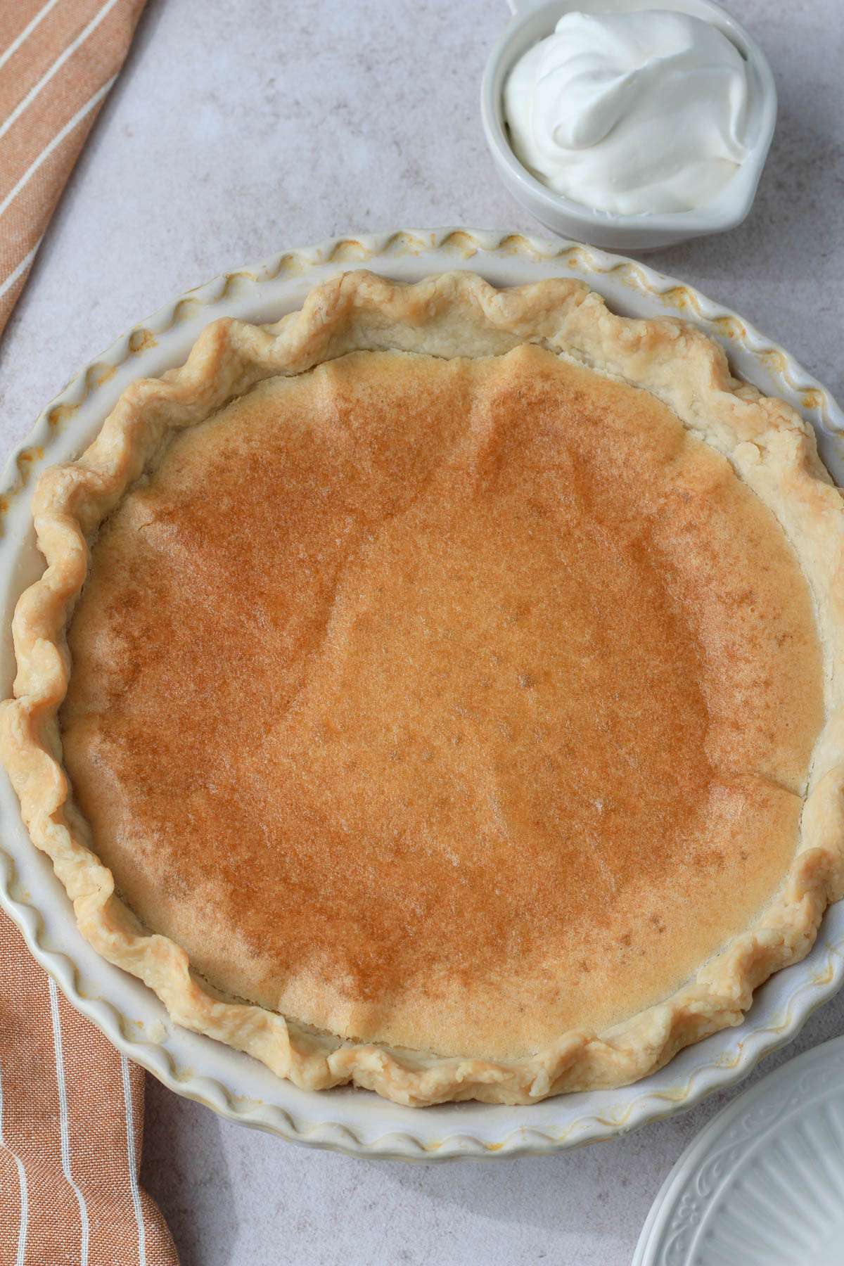A cream pie pan with chess pie in the middle and a small bowl of vegan whipped cream in the top right corner.