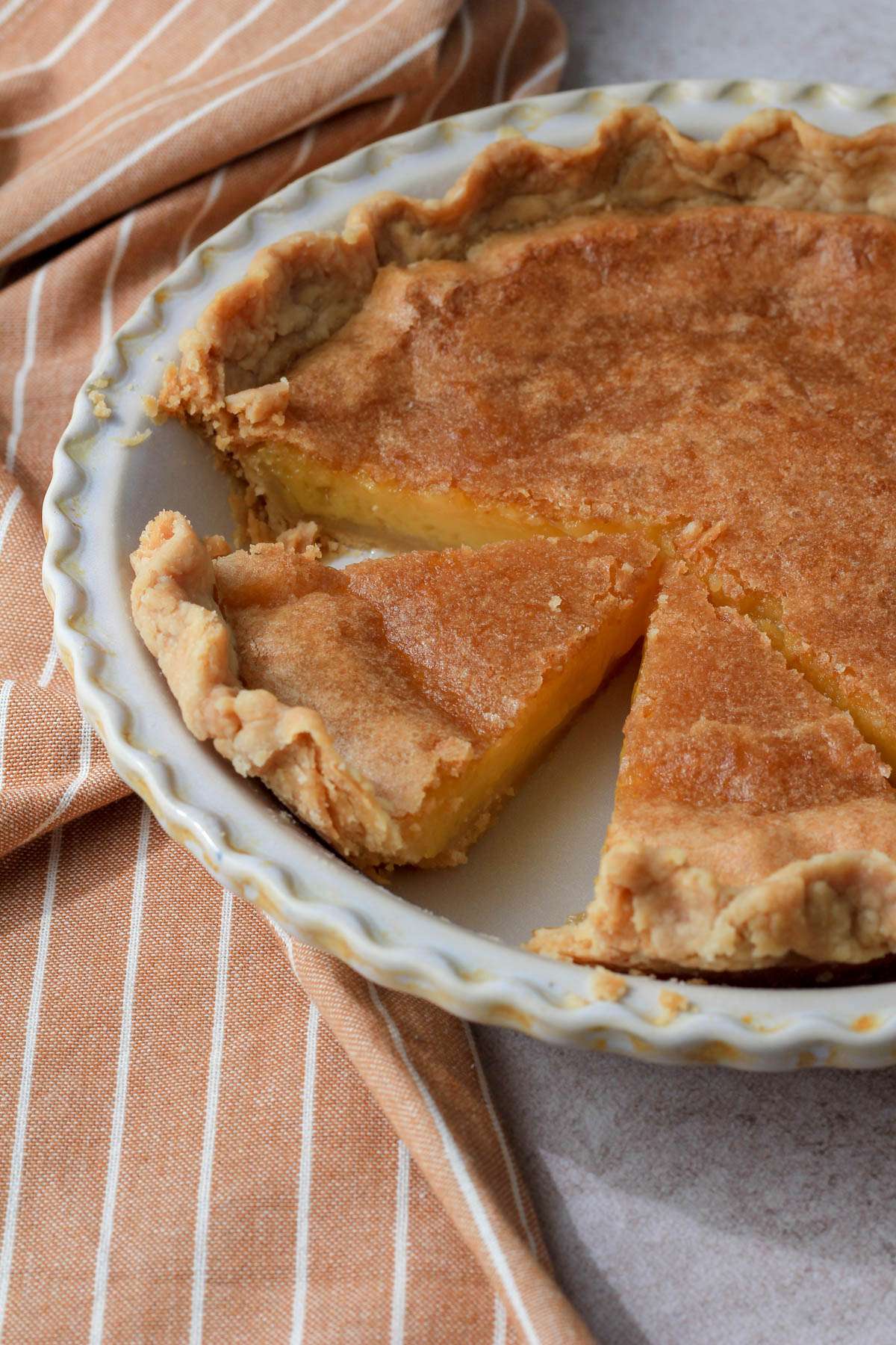 From the side, two slices of dairy-free chess pie in a cream pie pan detached from the rest of the pie.