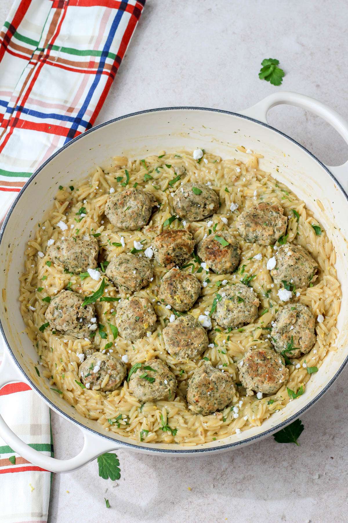 Greek turkey meatballs with creamy lemon orzo topped with feta and parsley on a cream counter.
