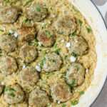 A close up of the right side of a white skillet with Greek turkey meatballs with creamy lemon orzo and dairy free feta.
