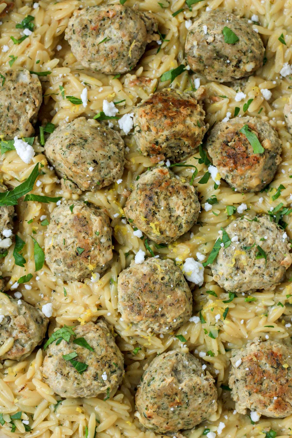 A close up of creamy lemon orzo topped with greek turkey meatballs and crumbled vegan feta.