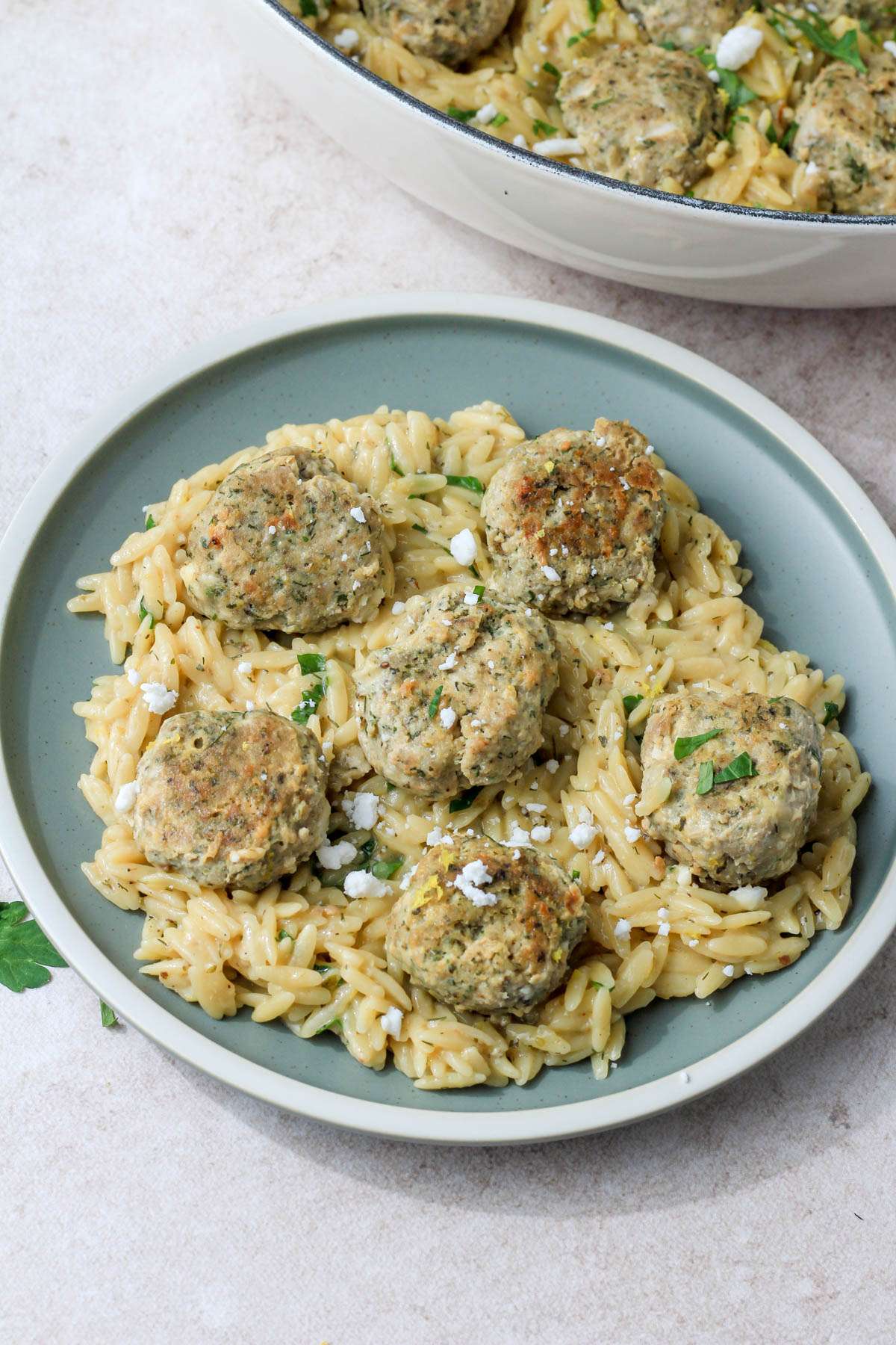 A green plate with a white rim and a serving of creamy lemon orzo topped with Greek turkey meatballs.