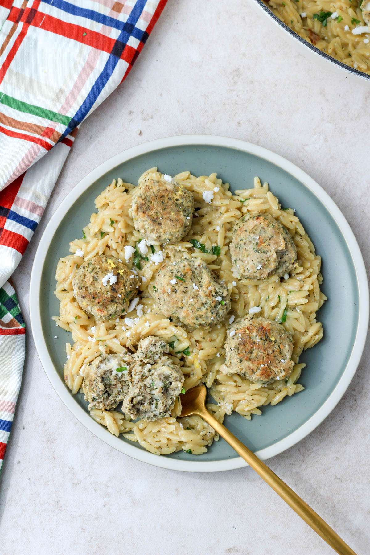 A top down picture of Greek turkey meatballs with creamy lemon orzo on a green plate with a white rim.