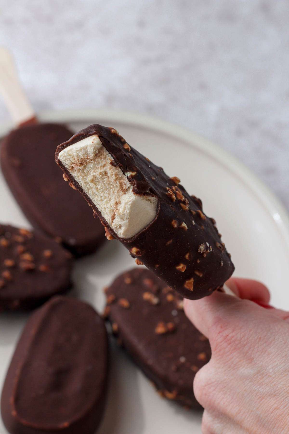 A hand holding a So Delicious mocha almond fudge dairy free ice cream bar with a bite taken out.