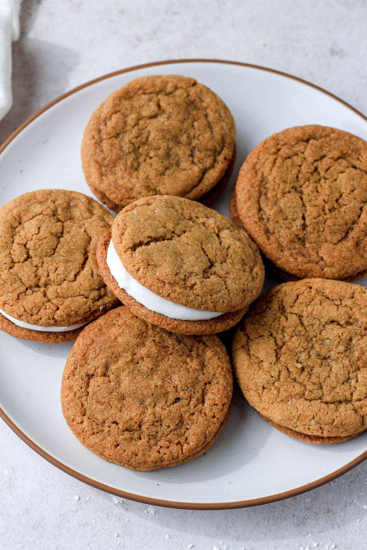 Six soft ginger cream pie cookies on a white plate with a brown rim and the middle cookie tipped to the left to expose the marshmallow cream icing.