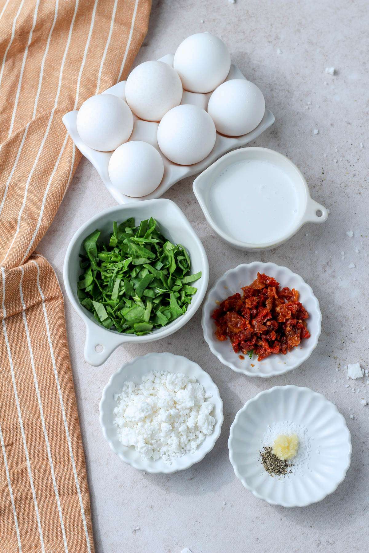 Ingredients for spinach, feta, and sun dried tomato egg bites on a tan counter.