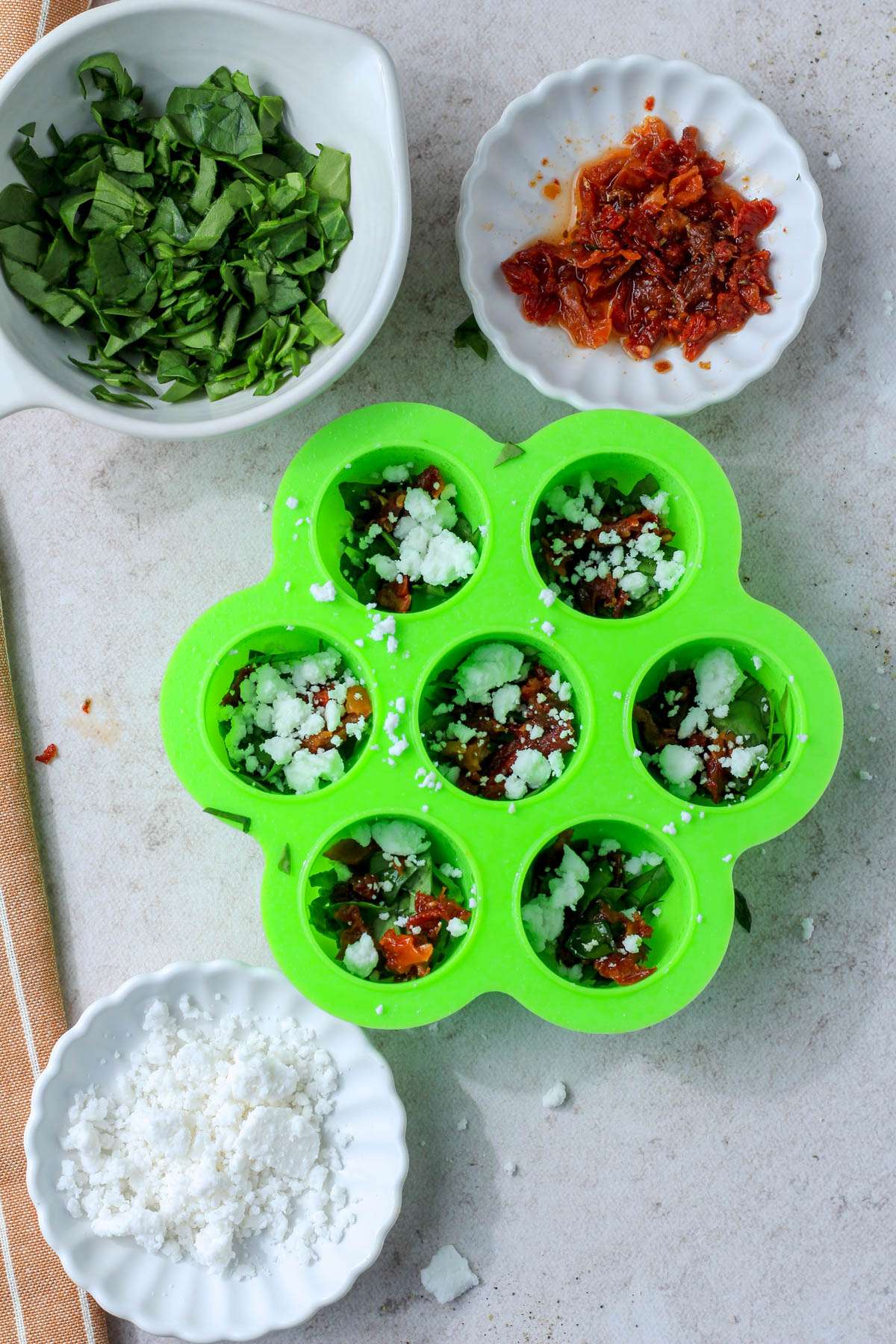 A green egg bites mold with spinach, feta, and sun dried tomatoes at the bottom.