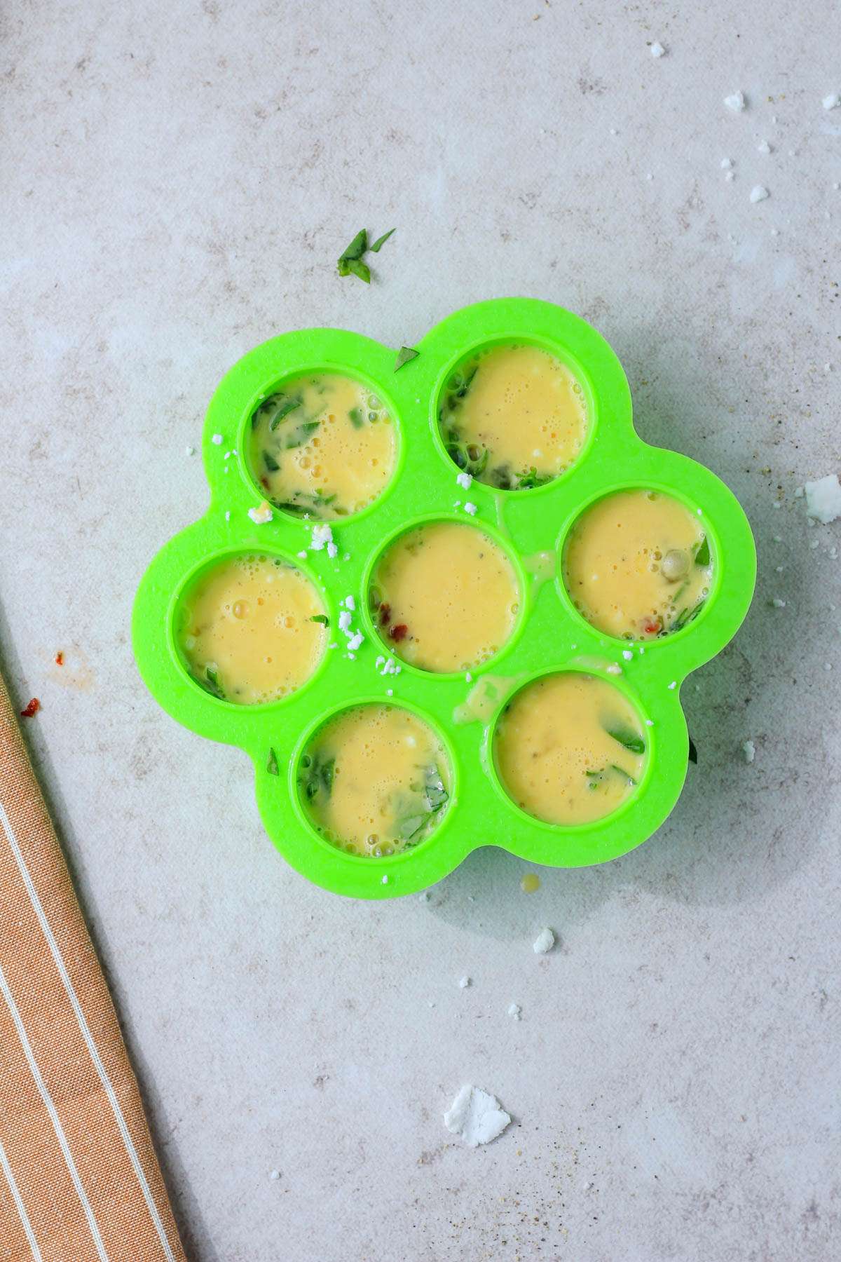 A green egg bites mold with spinach, feta, and sun dried tomato egg bites before cooking in the air fryer.
