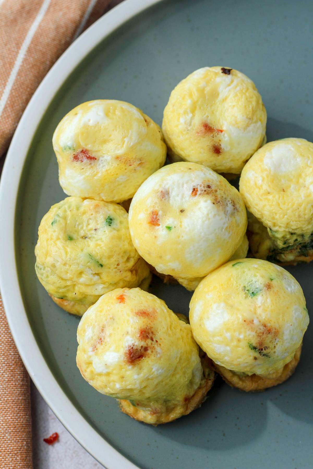 Dairy-free spinach and feta egg bites with sun dried tomatoes on a green plate with a cream rim.