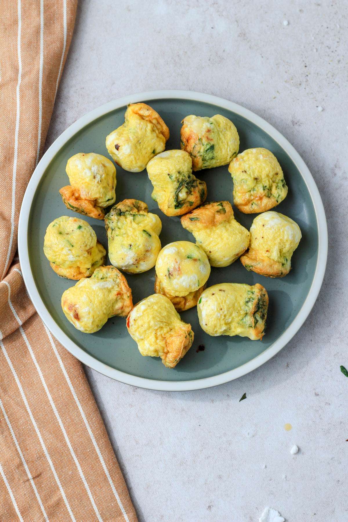 A green plate with spinach and feta egg bites on a tan counter.