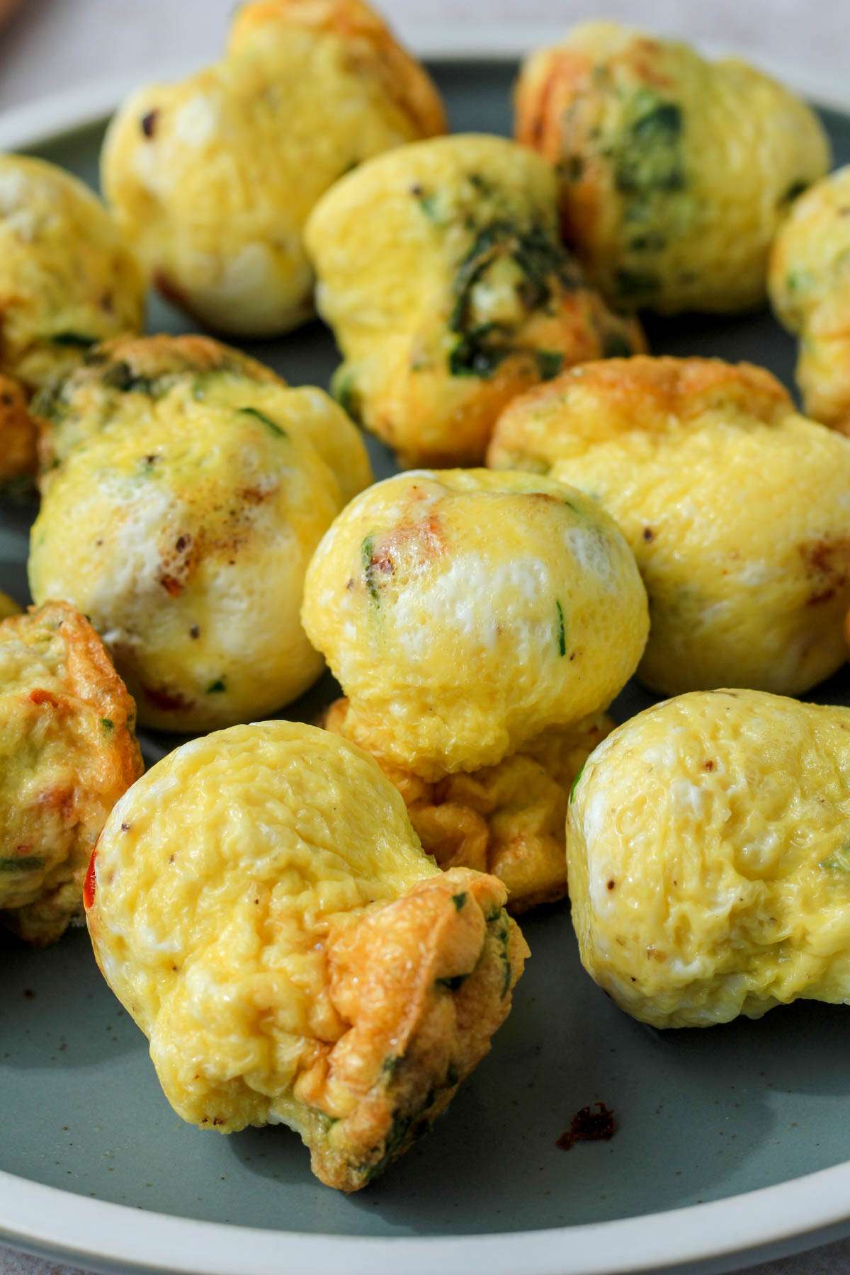 From the side, spinach and feta egg bites with sun dried tomatoes clustered on a green plate.