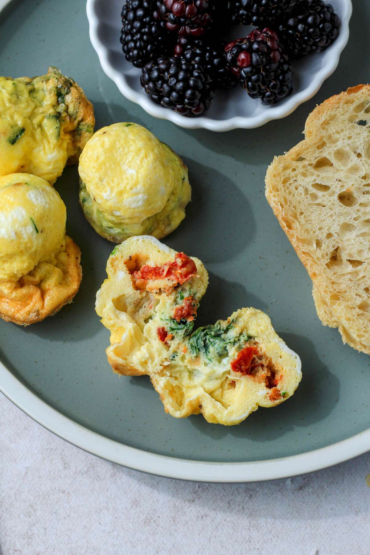 A spinach, feta, and sun dried tomato egg bite cut in half on a green plate.