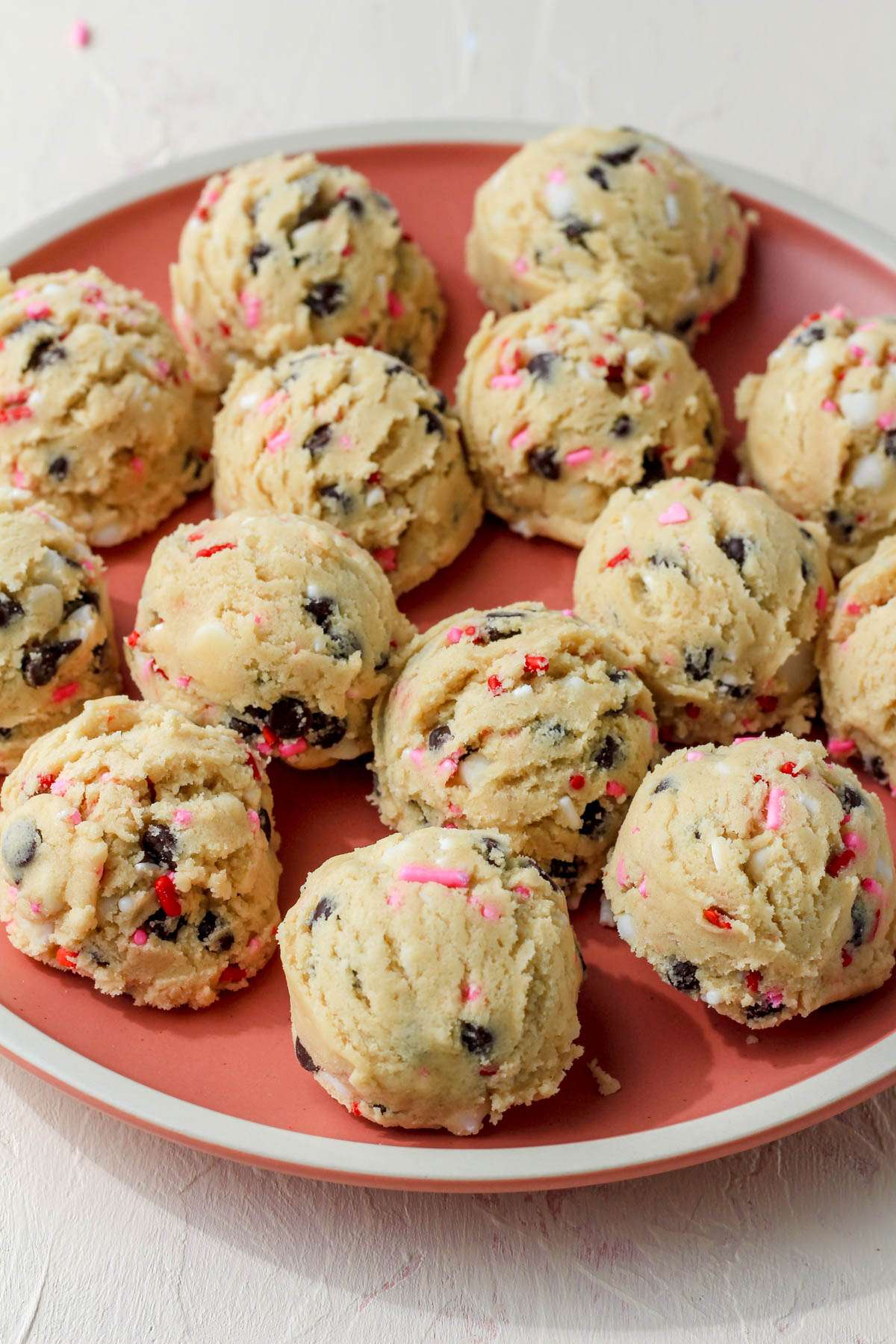 A pink plate with a cream rim and unbaked valentines day cookie dough.