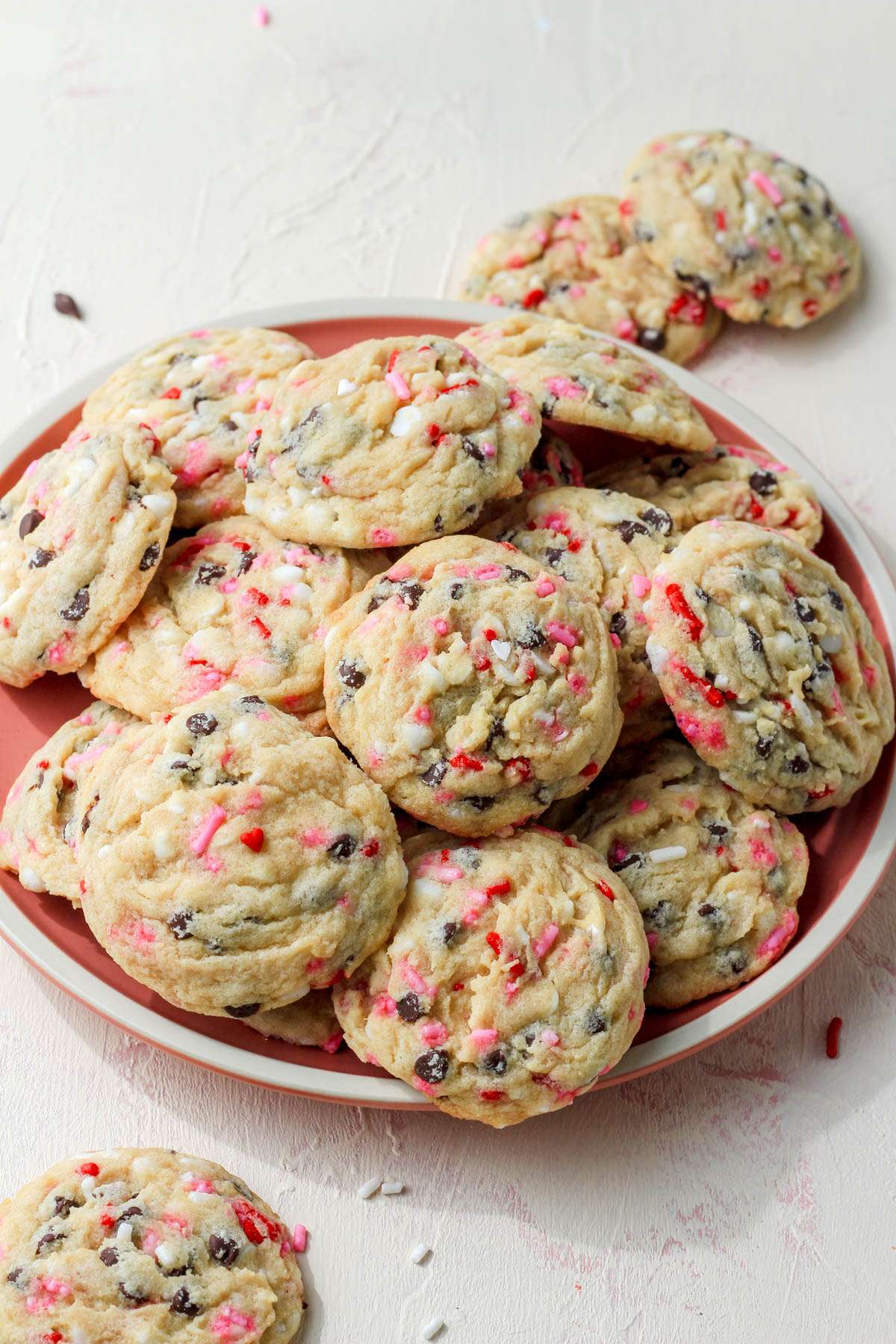 A cream counter with a pink plate topped with dairy-free chocolate chip cookies for valentines day with a few cookies spilled over on the sides of the plate.