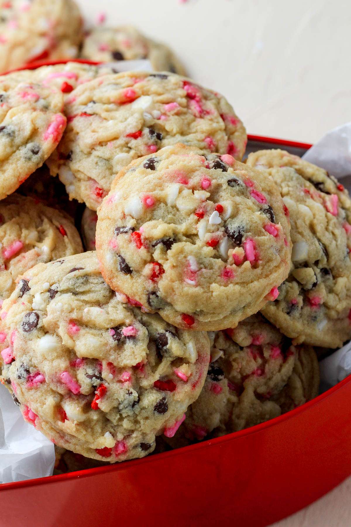 A red heart shaped cookie tin, from the side, filled with chocolate chip cookies for valentines day.