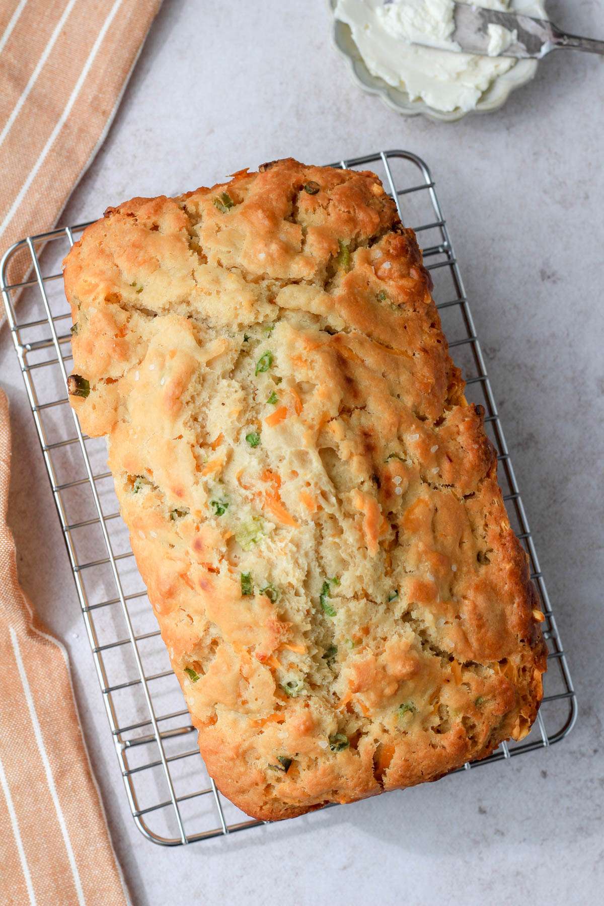 A wire cooling rack with a loaf of dairy-free cheddar and onion beer bread and a small dish of vegan butter in the top right.