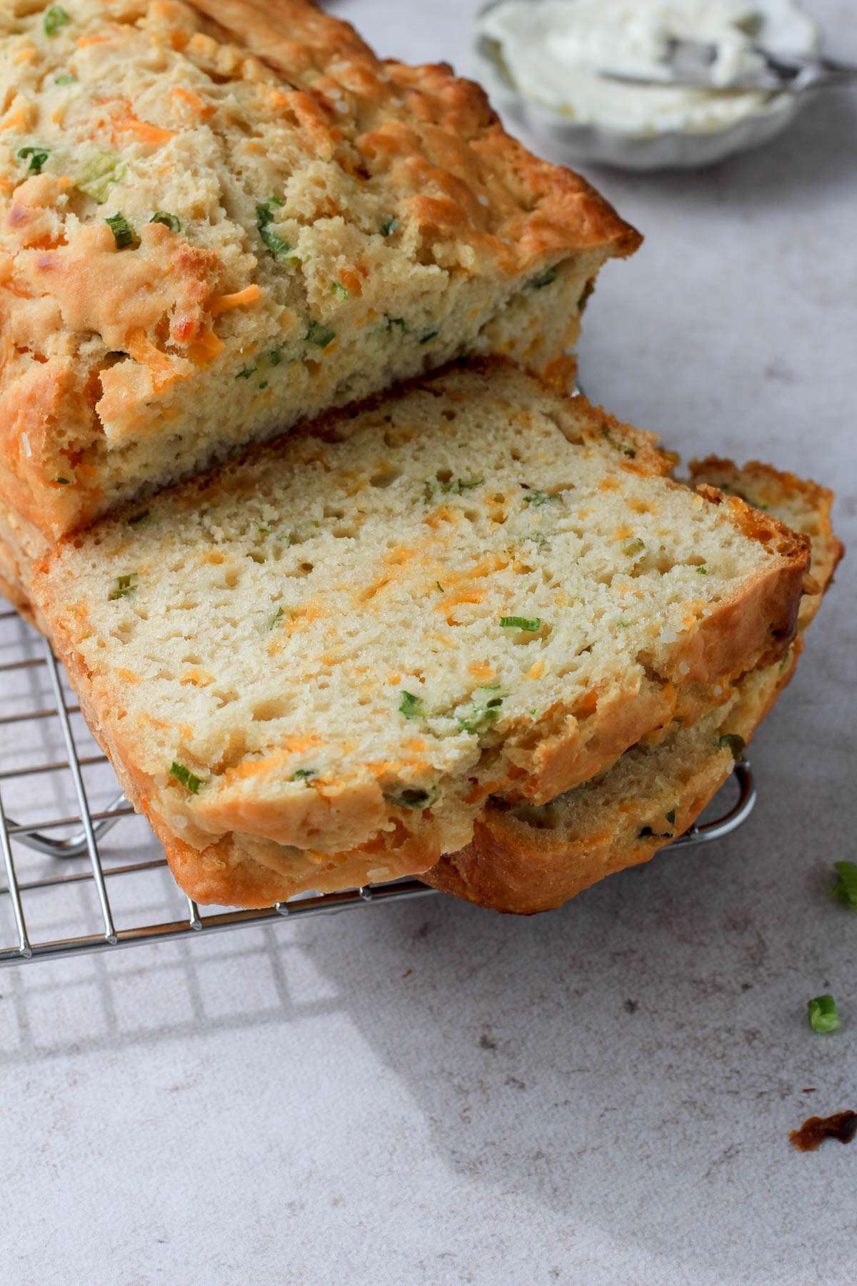From the side, slices of cheddar and onion beer bread on a wire cooling rack with a small dish of vegan butter in the back right.