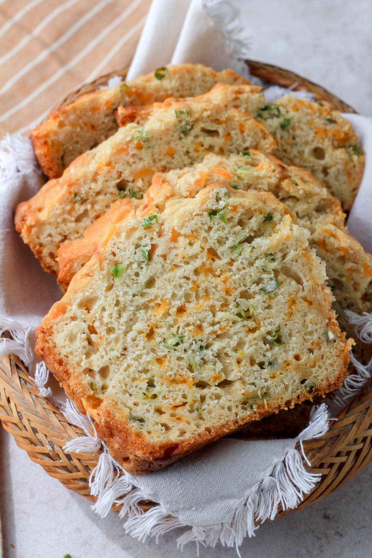 A brown basket with a cream towel topped with slices of cheddar and onion beer bread.