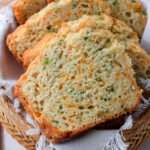 A close up of sliced cheddar and onion beer bread in a brown basket with a white towel.