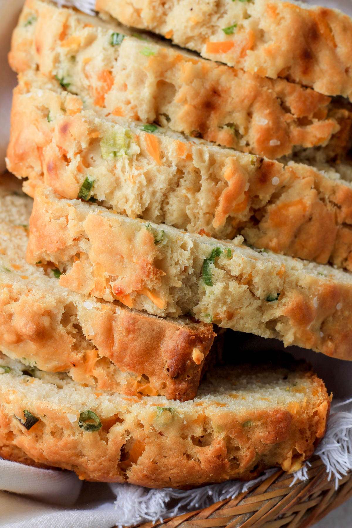 A close up of the tops of slices of cheddar and onion beer bread in a white towel lined bread basket.
