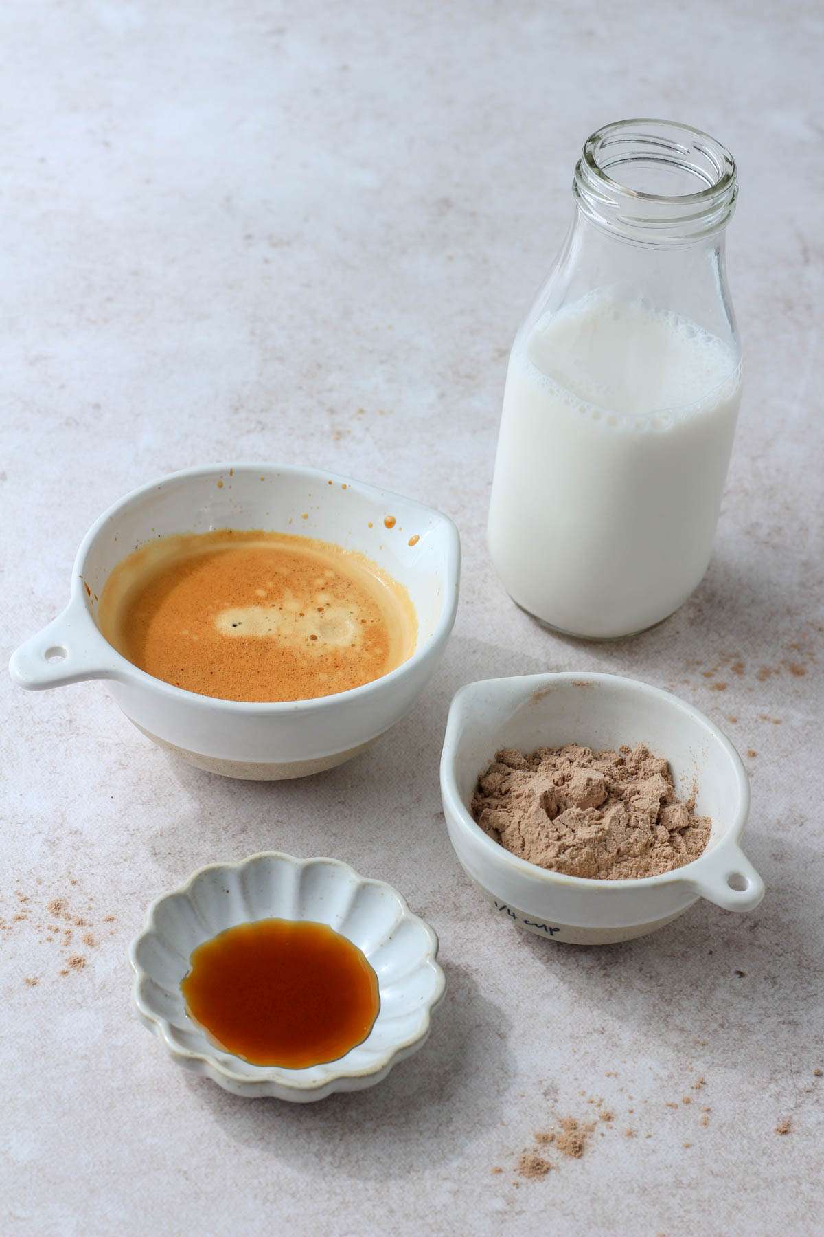 Ingredients for a chocolate protein almond milk shaken espresso on a tan counter.
