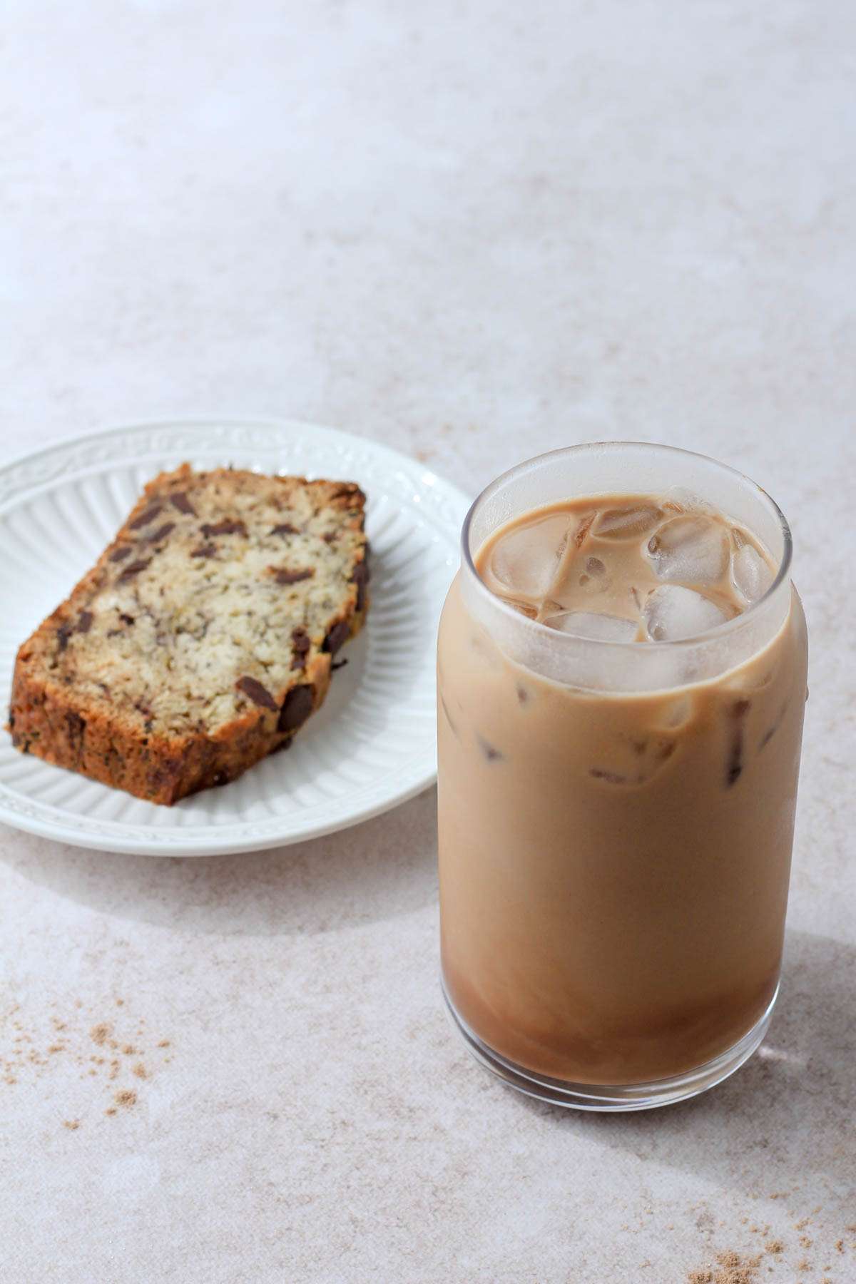 Vegan chocolate protein almond milk shaken espresso in front of a vegan slice of banana bread.
