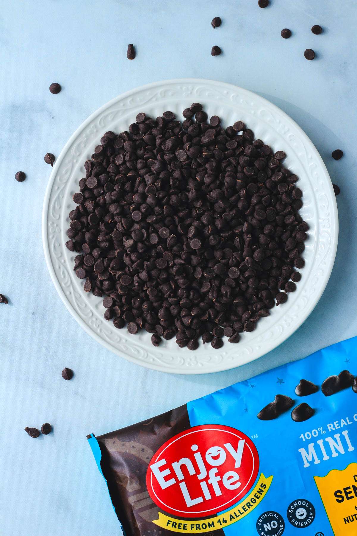 A bag of enjoy life semi sweet mini chocolate chips opened and poured on a white plate.
