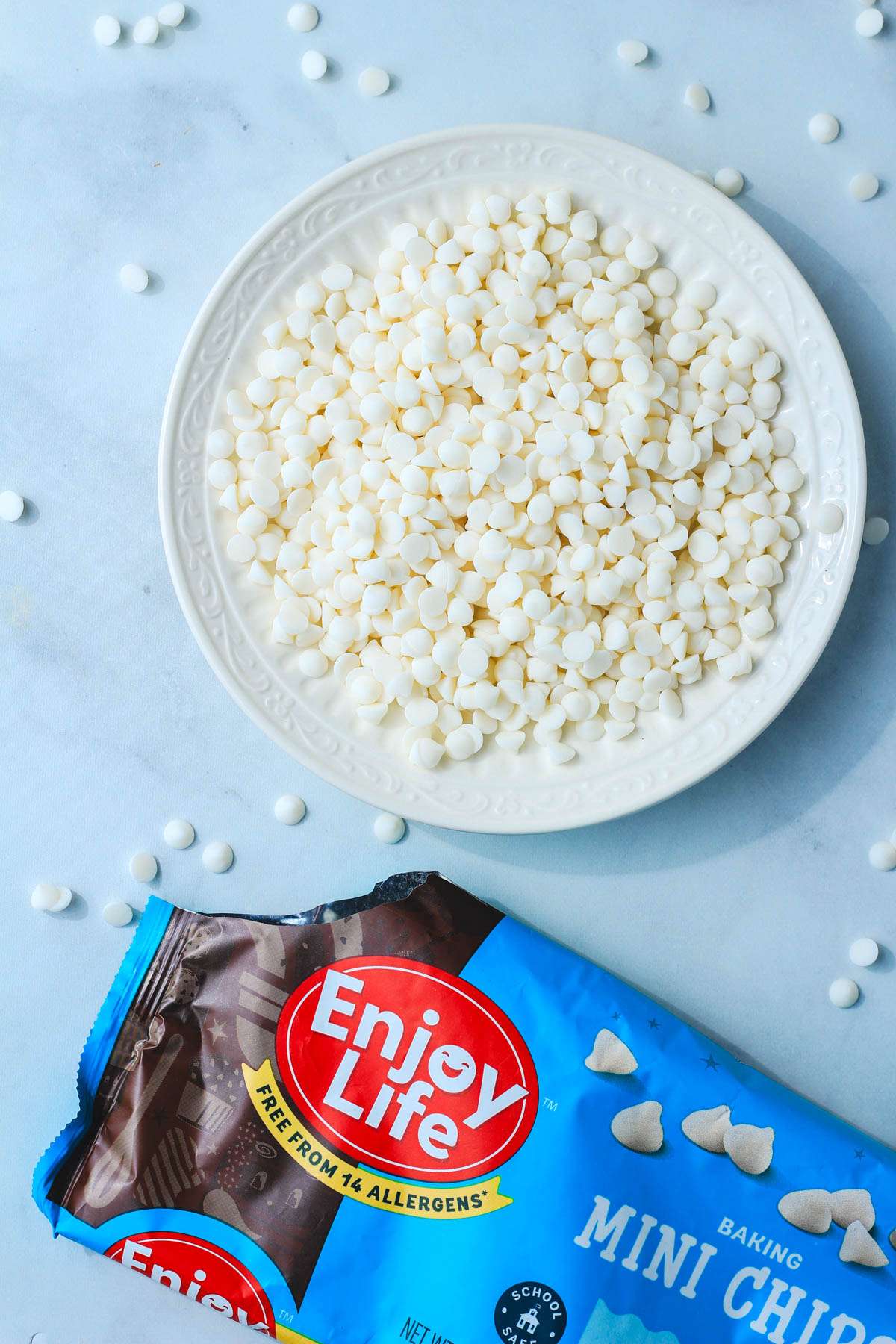 An open bag of enjoy life mini white chocolate chip poured onto a white plate.