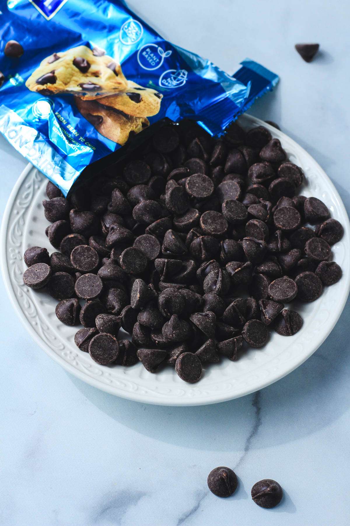 A white plate filled with dark chocolate chips coming from a blue bag.