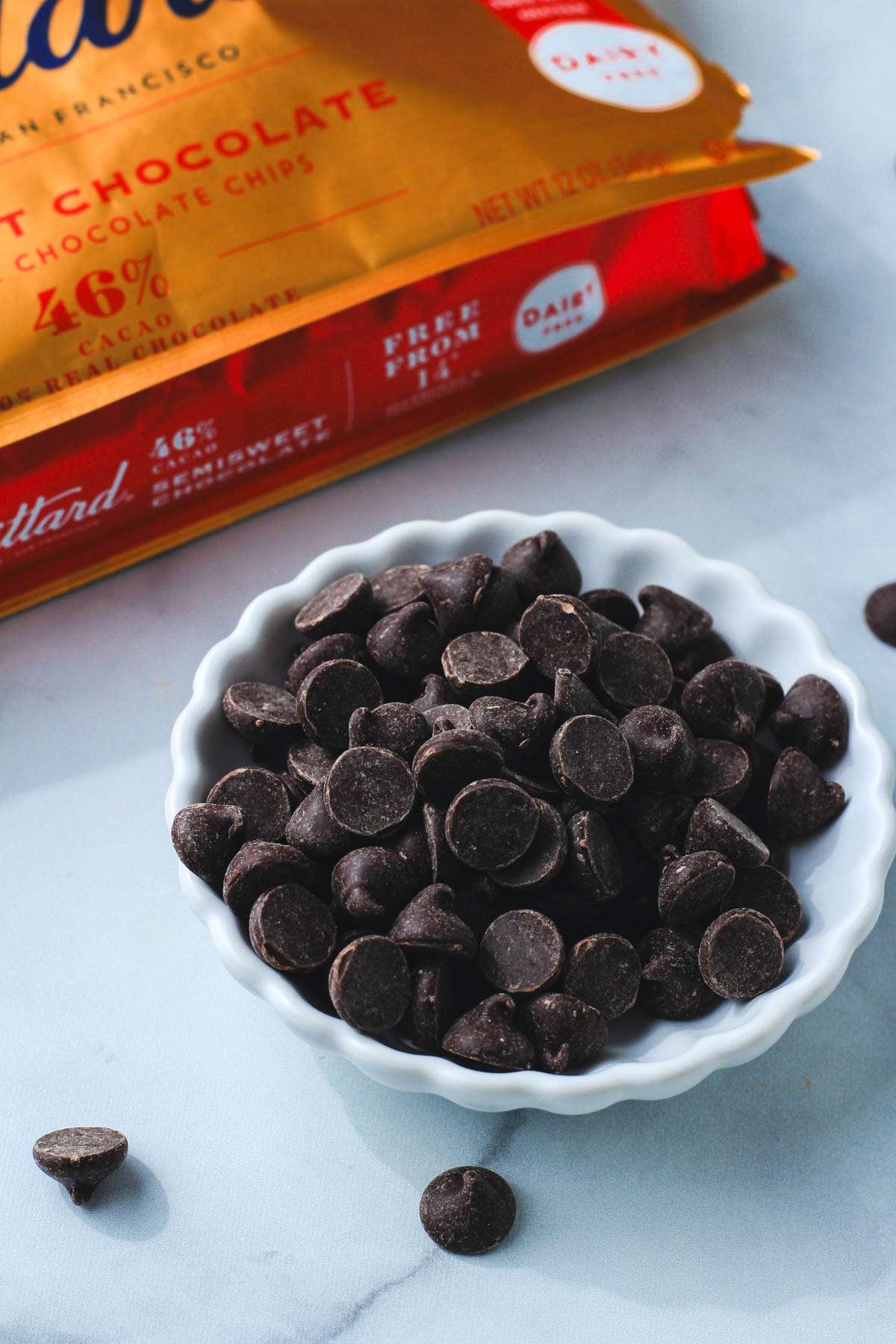 A white bowl of guittard dairy-free chocolate chips on a grey counter.