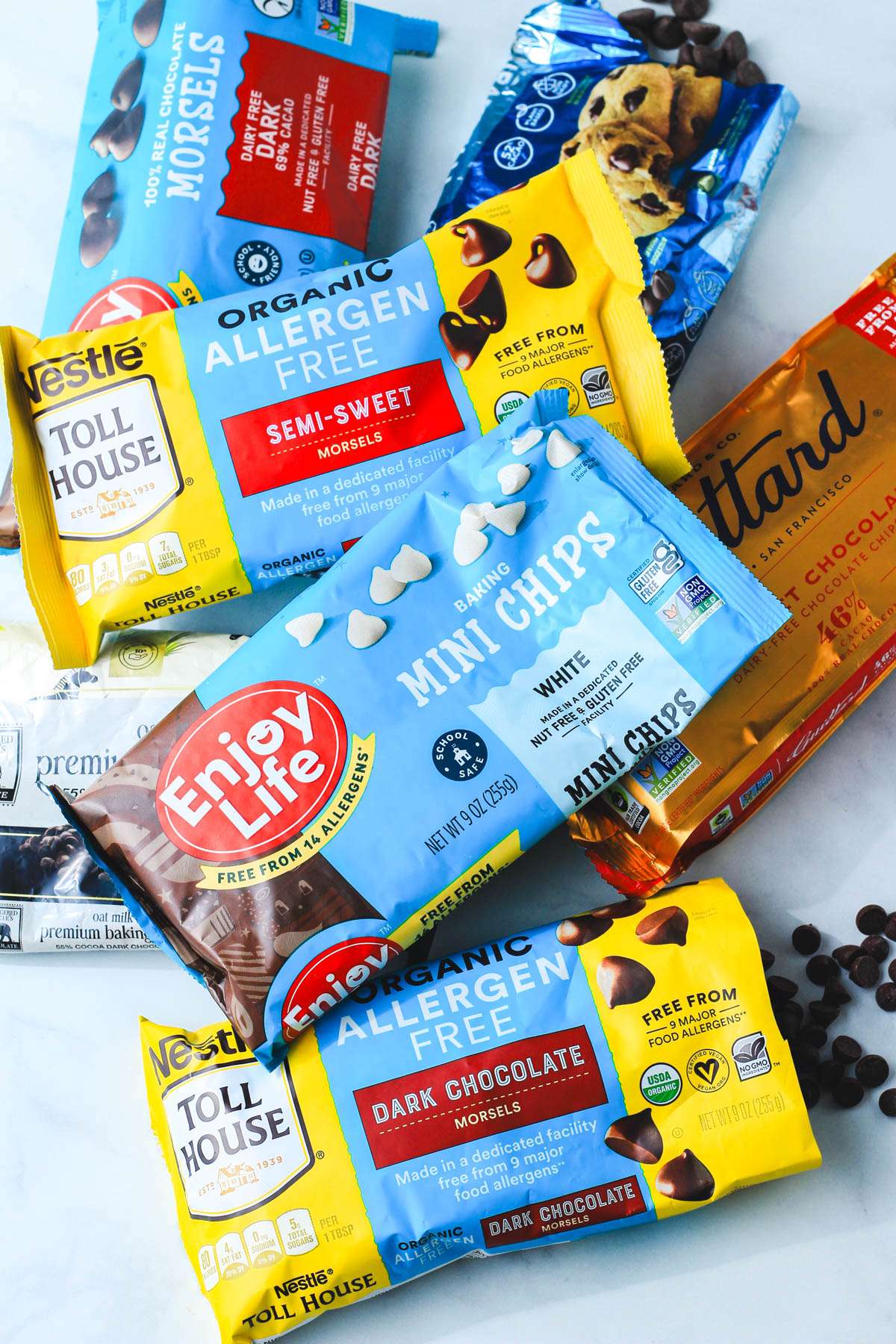 A pile of open bags of dairy-free chocolate chips on a grey counter.