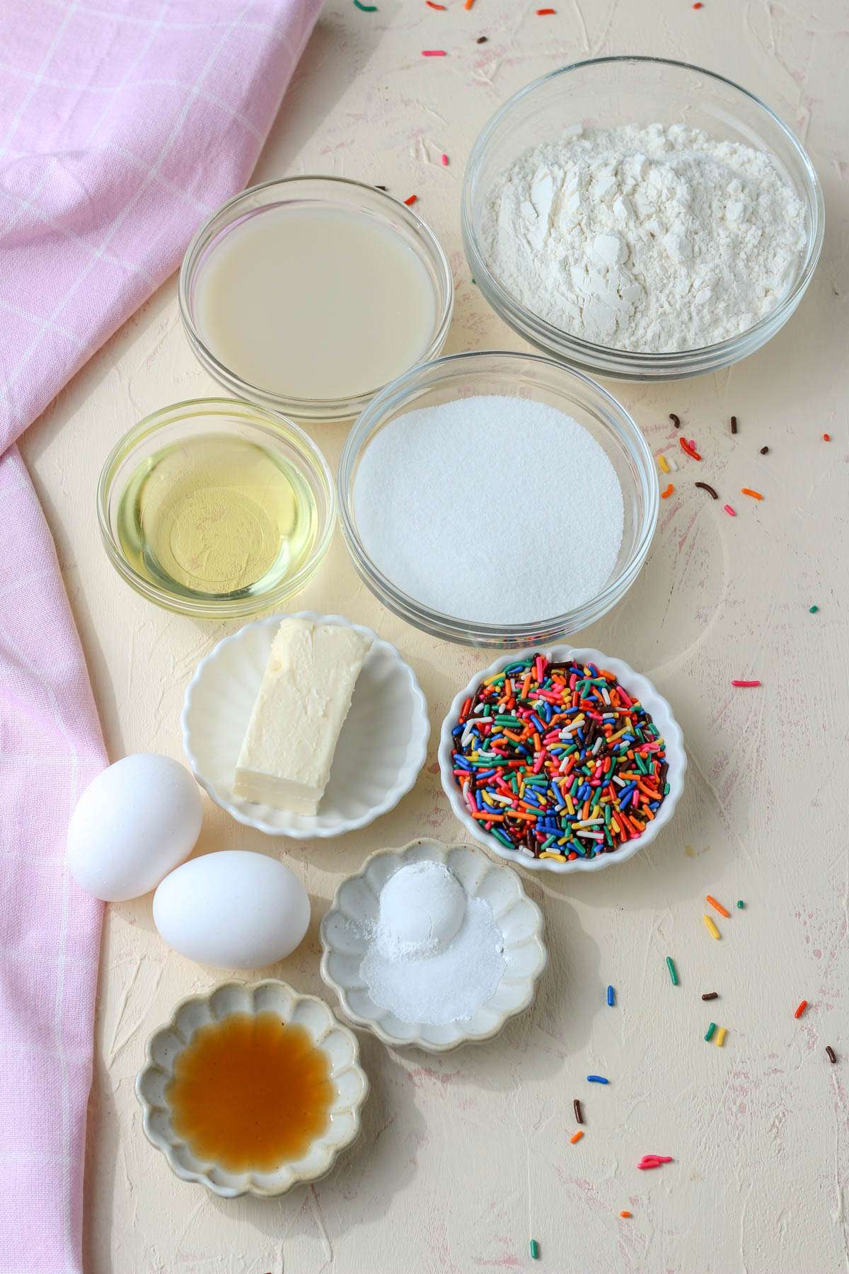 Ingredients for dairy-free funfetti cupcakes on a cream counter with a pink dish towel to the left.