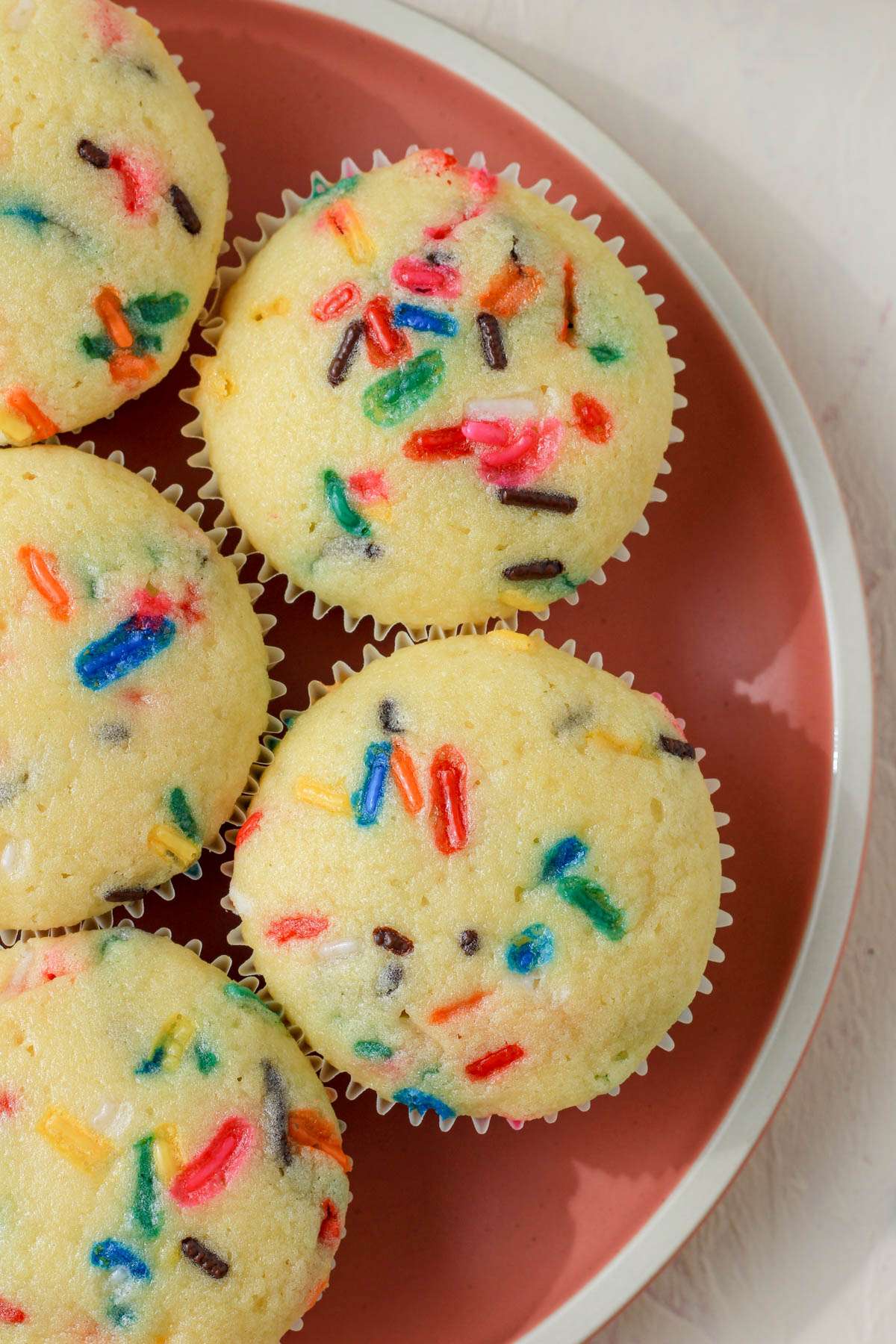 A top down image of a pink plate with dairy-free funfetti cupcakes before icing.