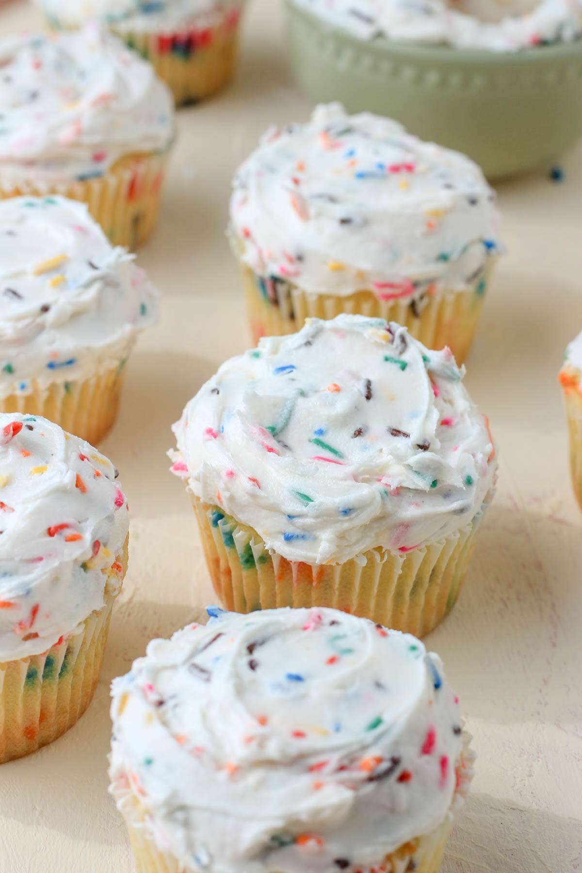 A cream counter with rows of iced dairy-free cupcakes with rainbow sprinkles.