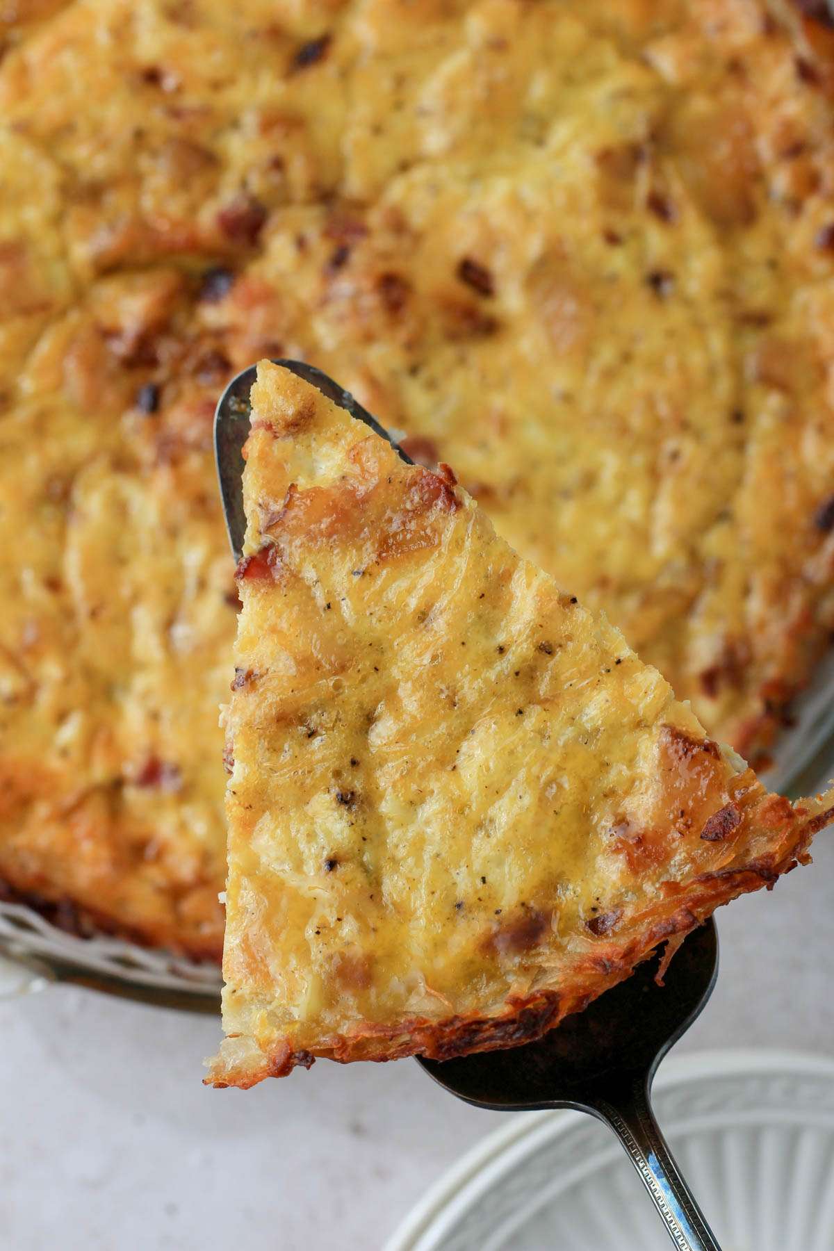 A silver server holding a slice of dairy-free hash brown crusted quiche over a pie pan with quiche.
