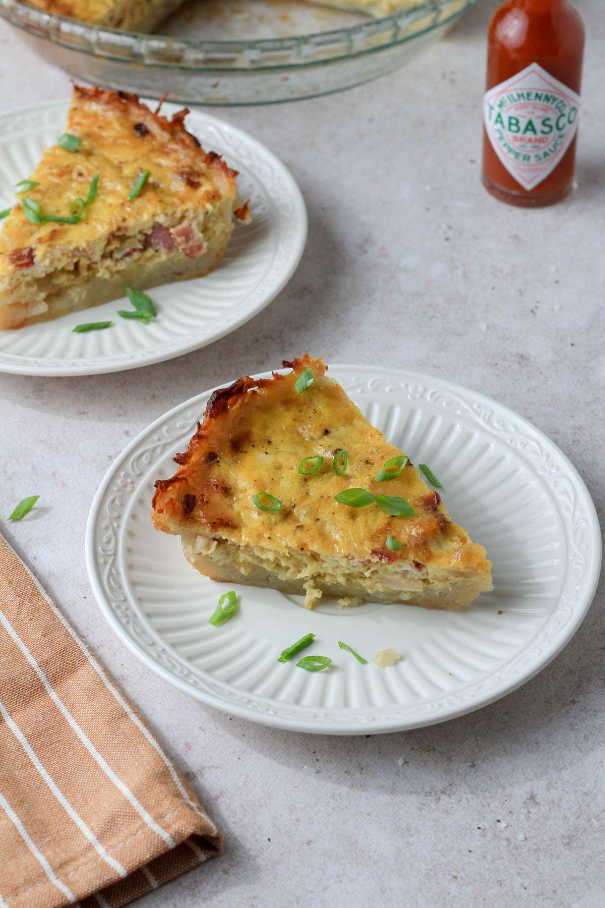 Two white plates on a tan counter with slices of dairy-free hash brown crusted quiche topped with green onion.