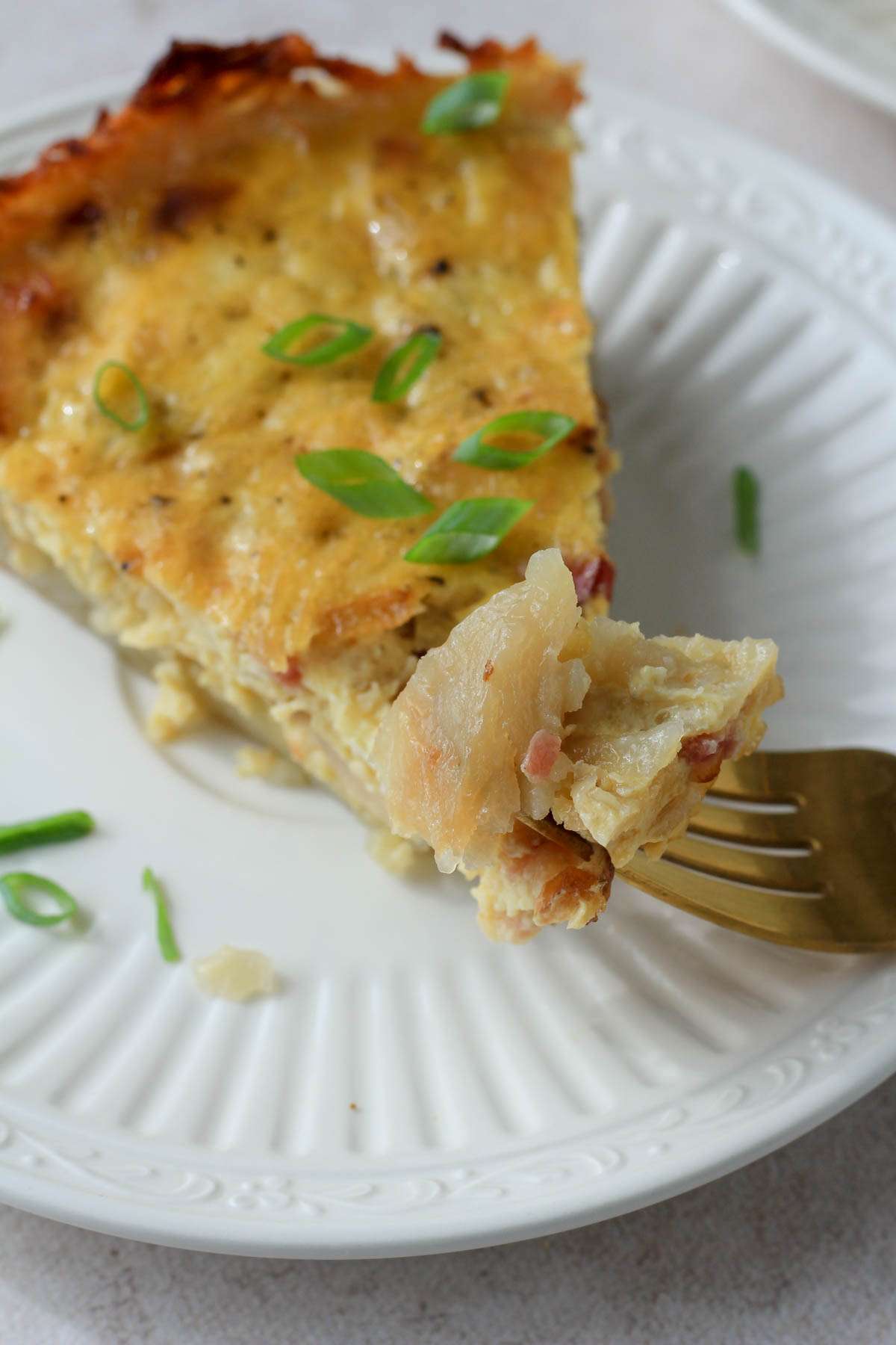 A white plate with a gold fork that has a bite of dairy-free hash brown crusted quiche.